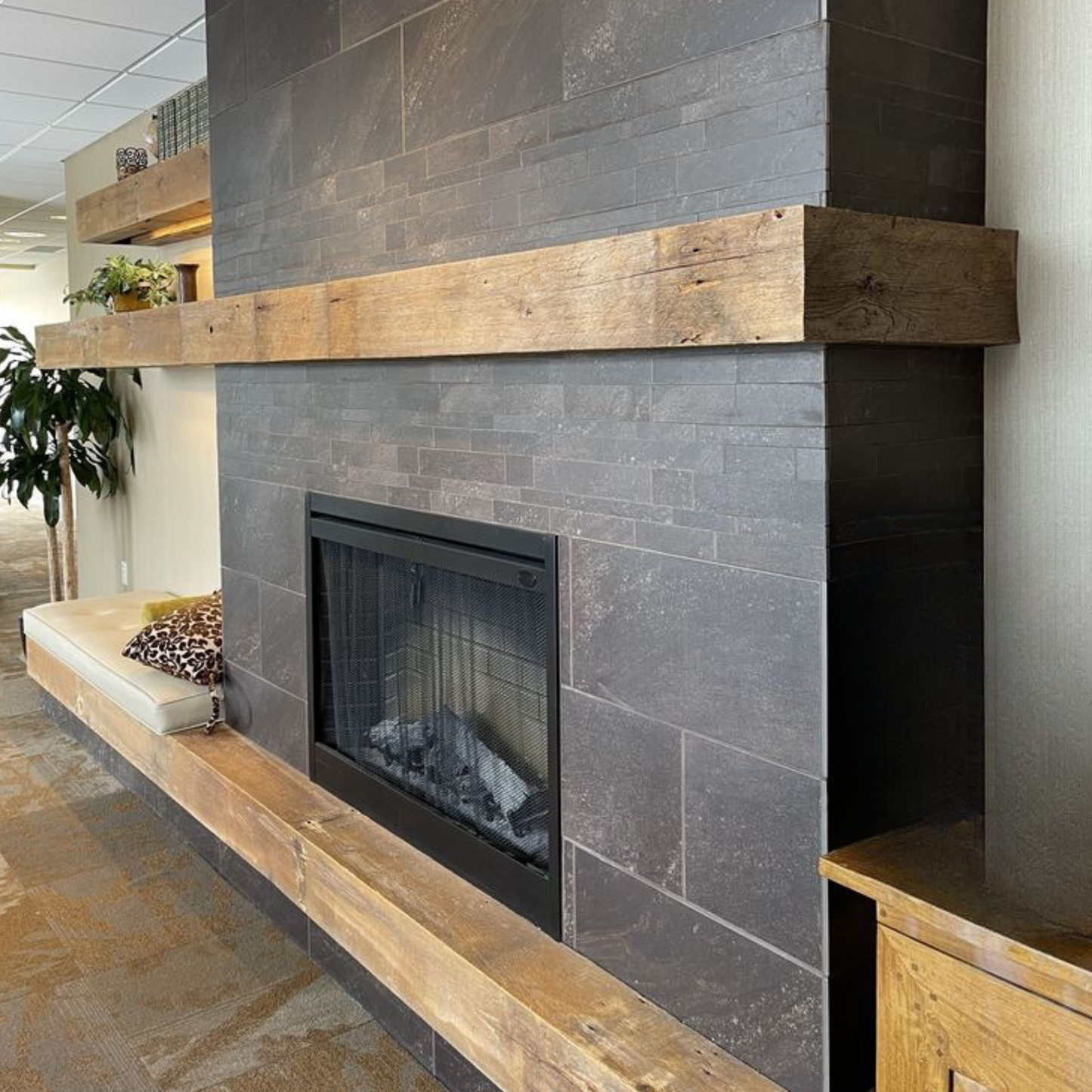 Obzidan kaminski vložek z ravno zasteklitvijo, obzidava je obložena z sivimi keramičnimi ploščicami, pod kaminskim vložkom pa je lesena polica