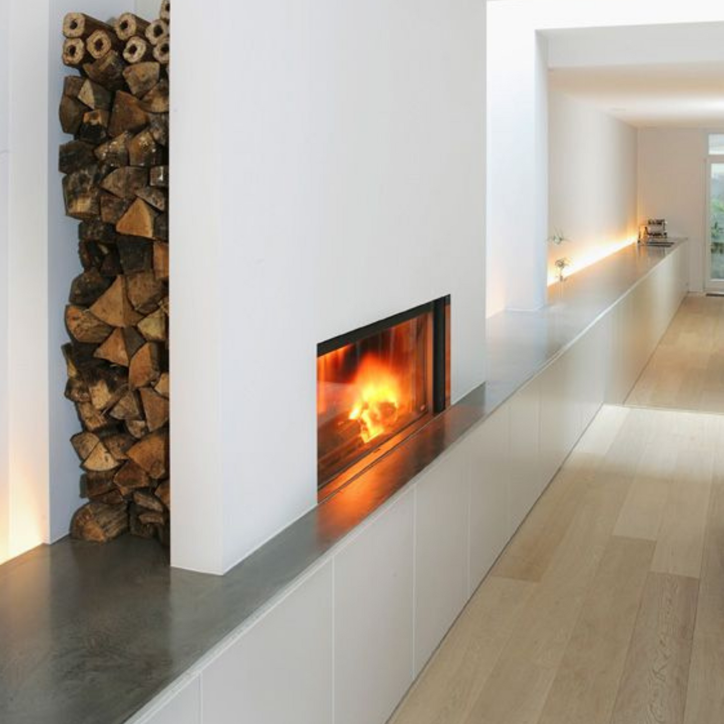 Obzidan kaminski vložek z ravno zasteklitvijo, obzidava je v beli barvi, na levi strani pa ima nišo za drva