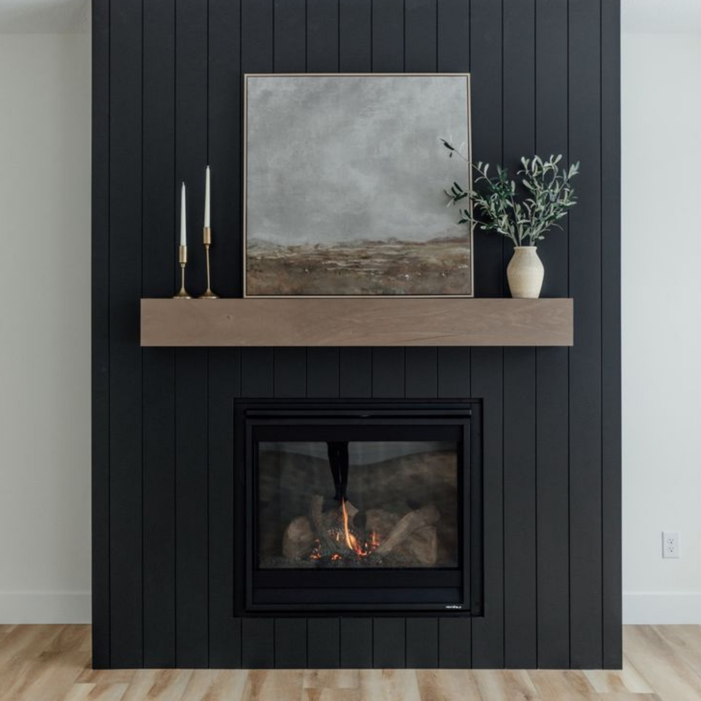 Obzidan kaminski vložek z ravno zasteklitvijo, obzidava je v črni barvi in ima nad kaminskim vložkom leseno polico